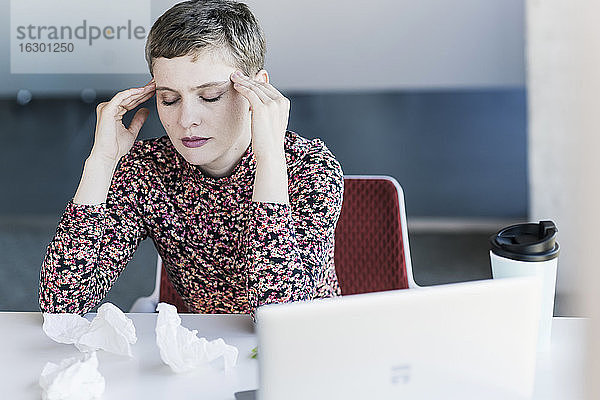Geschäftsfrau am Schreibtisch im Büro mit Kopfschmerzen