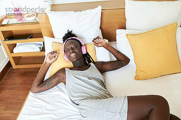 Frau hört Musik über Kopfhörer  während sie sich zu Hause auf dem Bett entspannt