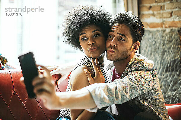 Paar spitzt die Lippen  während es ein Selfie mit dem Smartphone macht  während es im Café sitzt
