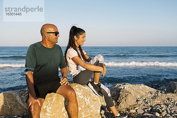 Älterer Mann sitzt mit Frau auf einem Felsen am Meer