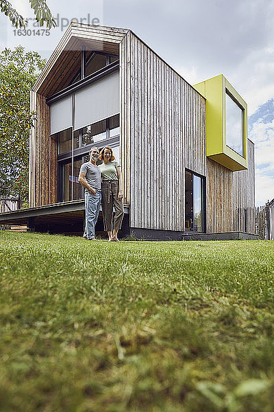 Paar stehend auf grasbewachsenem Land gegen kleines Haus im Hof