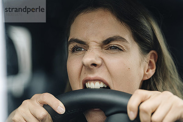 Nahaufnahme einer wütenden Frau  die ins Lenkrad beißt  während sie im Auto sitzt