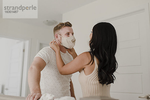 Frau bedeckt das Gesicht ihres Partners mit einer Schutzmaske während COVID-19