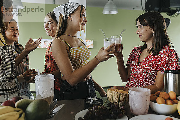 Teenager-Mädchen stehen in der Küche und probieren frische Frucht-Smoothies