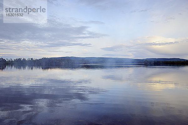 Schweden  Stroemsund  Sonnenuntergang an einem See und Rauch von einem Lagerfeuer