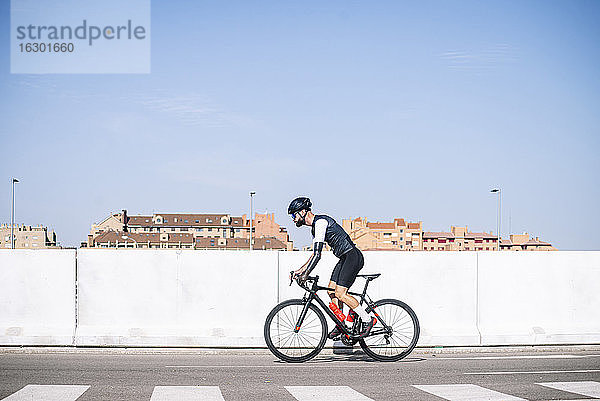 Männlicher amputierter Radfahrer  der mit dem Fahrrad auf der Straße gegen einen klaren blauen Himmel an einem sonnigen Tag fährt