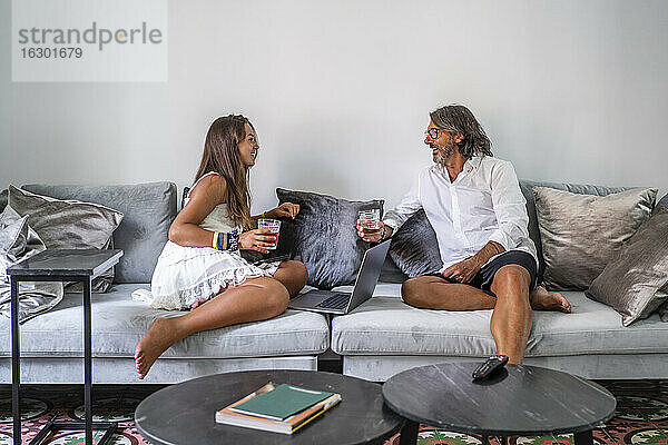 Lächelnder Vater und Tochter mit Getränken im Gespräch auf der Couch sitzend