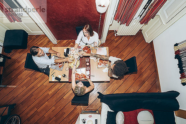 Freunde stoßen mit Weingläsern an  während sie auf einer Party zu Hause Pizza essen