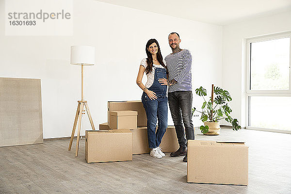 Ein glückliches Paar steht vor Kartons und einer elektrischen Lampe in einer neuen unmöblierten Wohnung