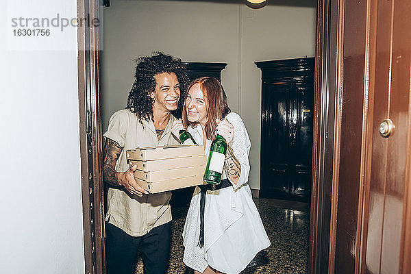 Fröhliche Freunde mit Bierflaschen und Pizzakartons am Eingang eines Hauses während einer Party