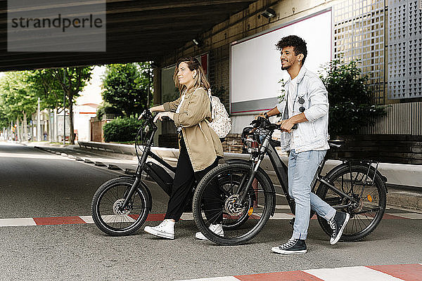 Ehepaar überquert Straße mit Elektrofahrrädern in der Stadt