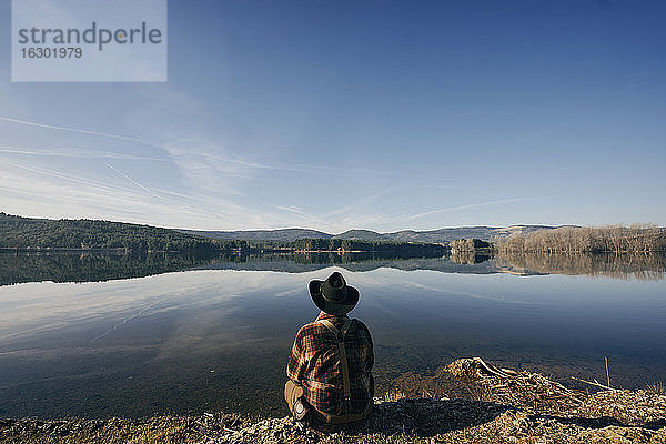 Buschmann schaut auf den See  während er unter blauem Himmel sitzt