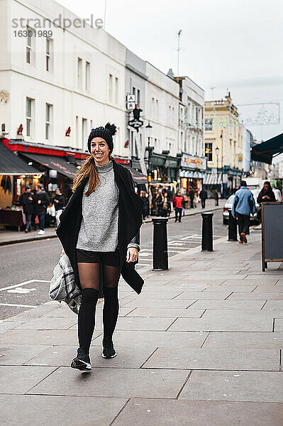 Frau lächelnd beim Gehen auf der Straße in der Stadt im Winter