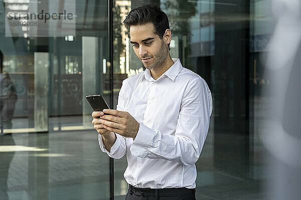 Männlicher Berufstätiger  der ein Smartphone benutzt  während er im Büro am Fenster steht