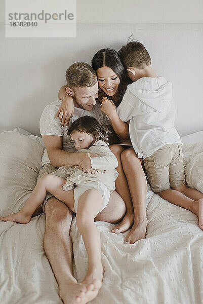 Lächelnde Eltern  die ihre Kinder umarmen  während sie auf dem Bett im Schlafzimmer sitzen