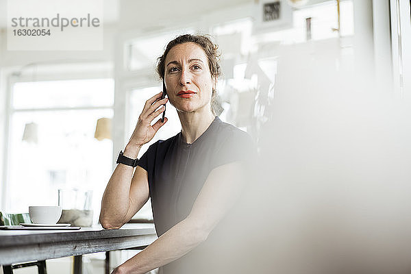 Selbstbewusste Geschäftsfrau  die am Tisch sitzend über ein Smartphone spricht