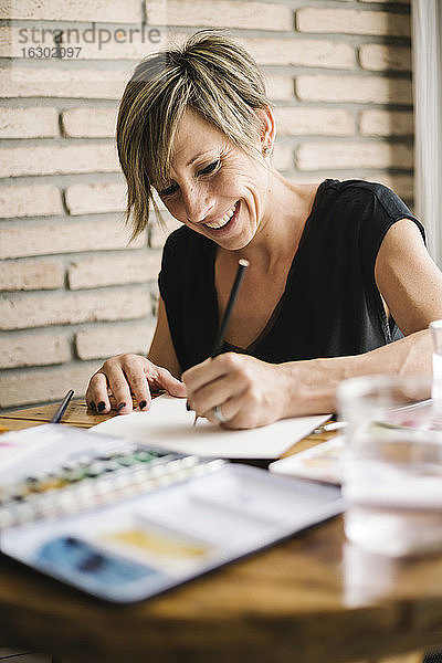 Lächelnde Frau hält Zeichnung auf Papier zu Hause
