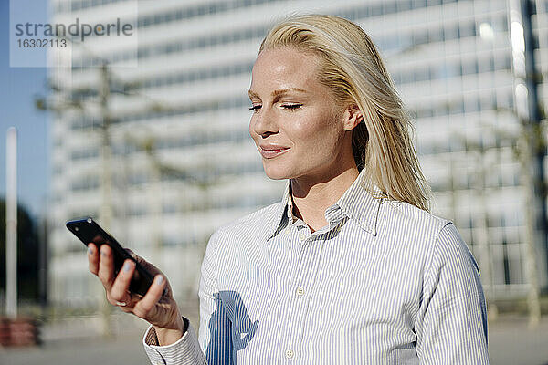 Schöne blonde Unternehmerin mit Smartphone in der Stadt an einem sonnigen Tag
