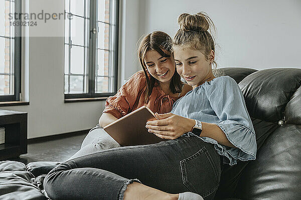 Freunde benutzen ein digitales Tablet  während sie sich zu Hause auf dem Sofa entspannen