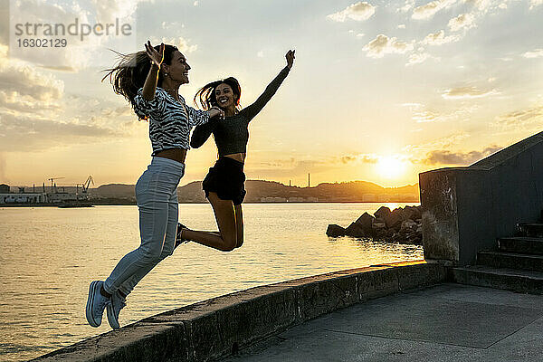 Junge Frauen  die bei Sonnenuntergang auf der Promenade springen