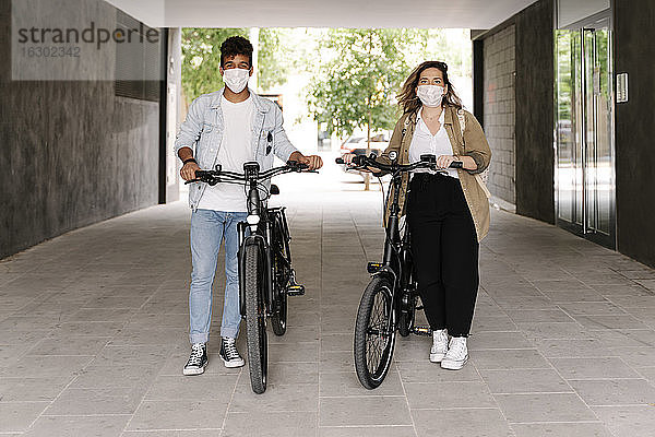 Pärchen mit Gesichtsschutzmasken steht mit Elektrofahrrädern auf dem Gehweg