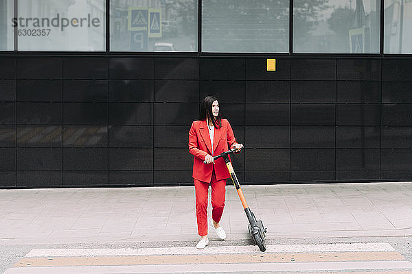 Geschäftsfrau zu Fuß mit Elektro-Scooter in der Stadt