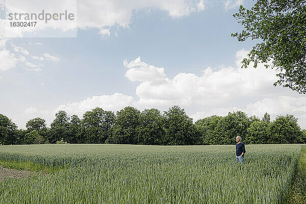 Mann mit Händen in den Taschen steht in einem landwirtschaftlichen Feld