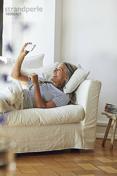Frau benutzt Smartphone auf Sofa im Wohnzimmer