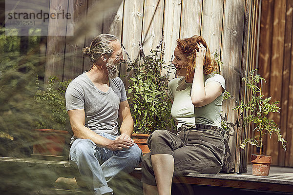 Fröhliches Paar  das sich unterhält  während es bei Topfpflanzen vor einem kleinen Haus sitzt