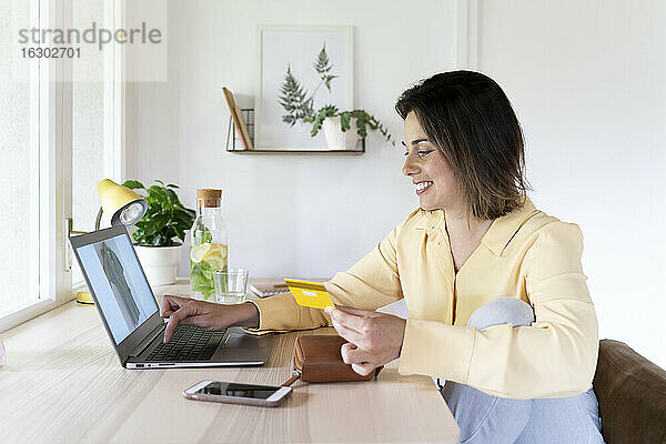 Glückliche schöne junge Frau  die einen Laptop zum Online-Shopping zu Hause benutzt