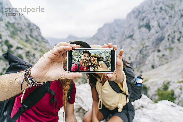 Paar  das ein Selfie mit dem Handy macht  während es auf einem Felsen an der Ruta Del Cares sitzt  Asturien  Spanien