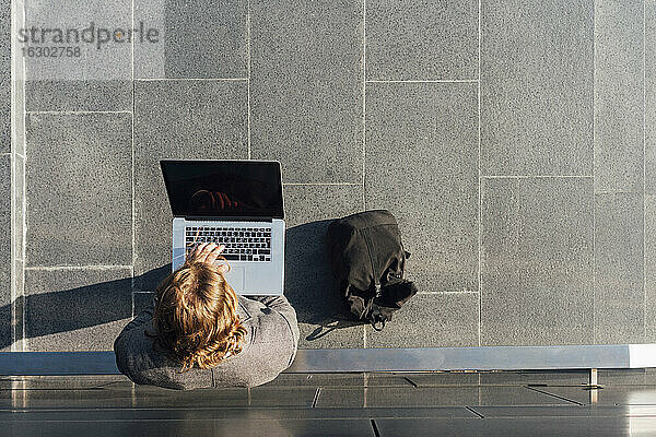 Junge männliche Fachkraft  die einen Laptop benutzt  während sie an einer Wand in der Innenstadt an einem sonnigen Tag steht