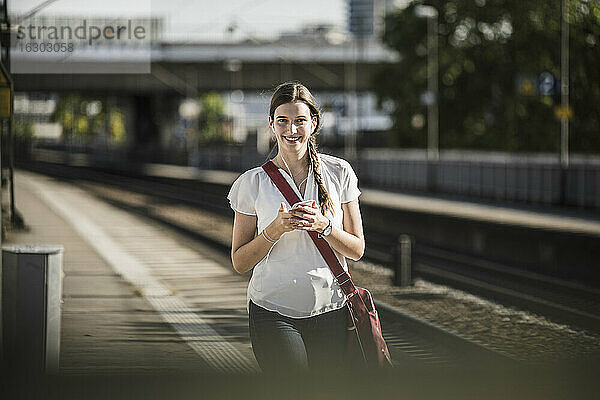 Schöne junge Frau hört Musik über ihr Handy  während sie auf dem Bahnsteig spazieren geht
