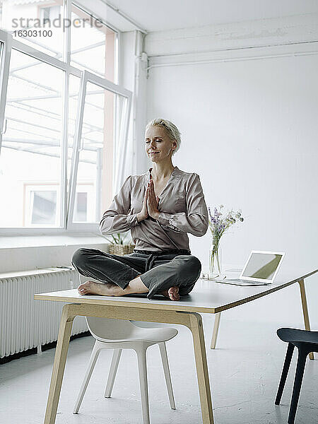 Geschäftsfrau meditiert auf dem Schreibtisch in einem Loftbüro sitzend
