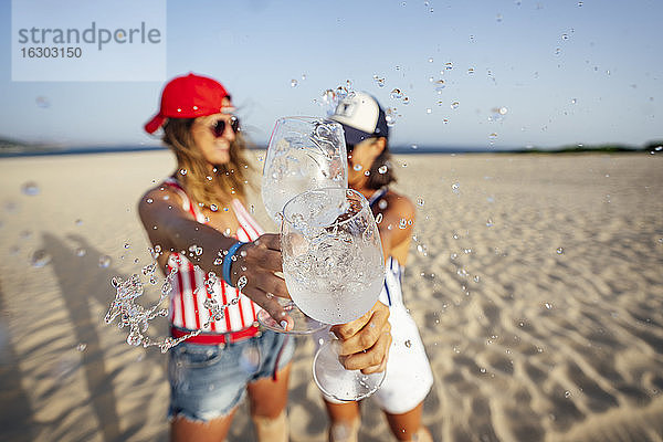 Mid erwachsenen weiblichen Freunde spritzen Getränk während Toasting am Strand an einem sonnigen Tag