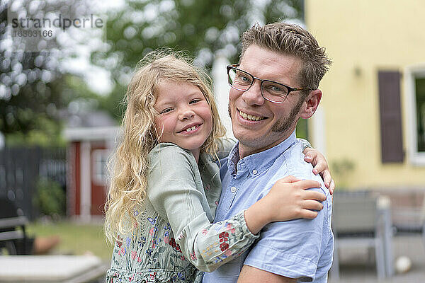 Lächelnder Mann mit blonder Tochter im Hinterhof
