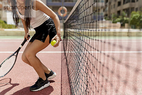 Eine Tennisspielerin hält einen Schläger und einen Ball  während sie am Netz steht