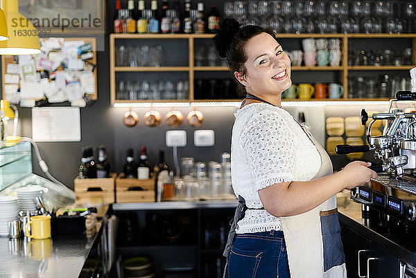 Lächelnde weibliche Barista  die bei der Arbeit in einem Café an der Kaffeemaschine steht