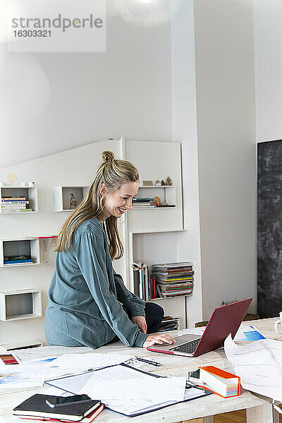 Lächelnde Frau mit Laptop auf dem Schreibtisch im Home Office