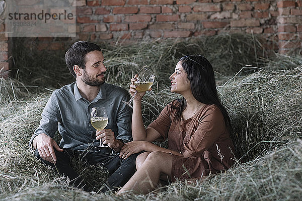 Glückliches Paar mit Cocktails auf Heu in einer Scheune sitzend