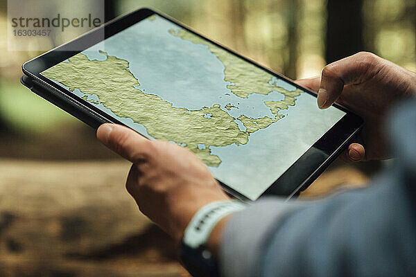 Nahaufnahme eines erwachsenen Mannes  der mit seinen Händen eine Karte über einem digitalen Tablet im Wald analysiert