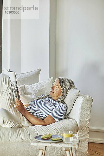 Frau liest Zeitschrift auf Sofa im Wohnzimmer