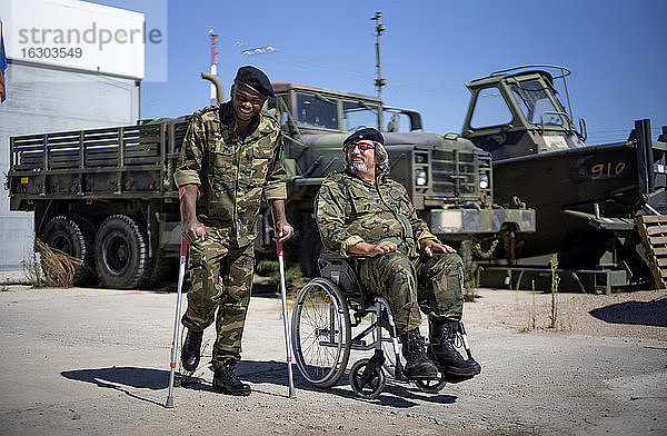 Junger Militäroffizier mit Krücken lächelt  während sein Kollege an einem sonnigen Tag im Rollstuhl sitzt