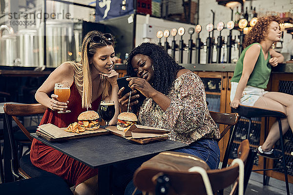 Glückliche Freundinnen mit Smartphone beim Burgeressen in einer Kneipe