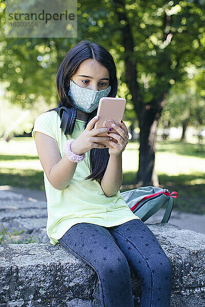 Mädchen mit Gesichtsmaske telefoniert in einem öffentlichen Park