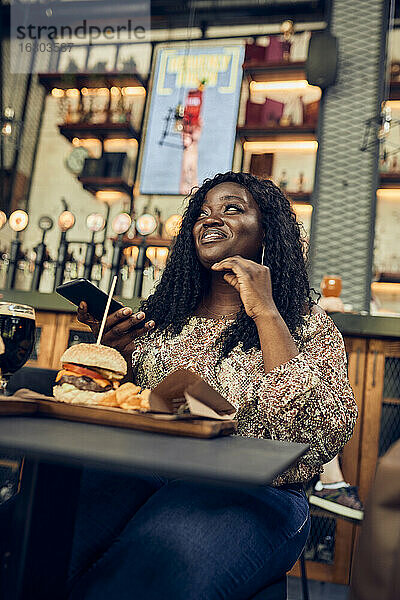 Lächelnde Frau isst einen Burger in einer Kneipe