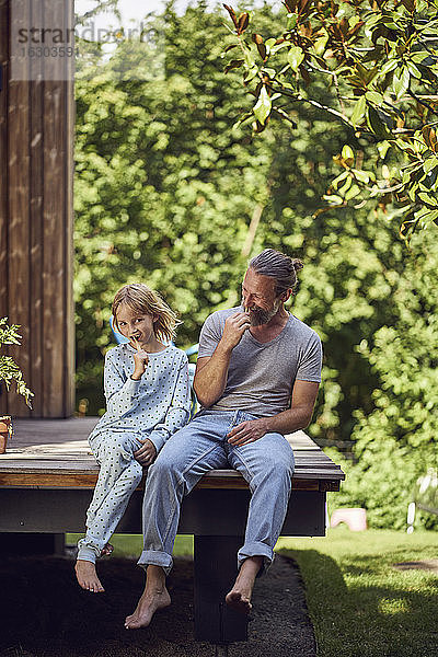 Vater und Tochter putzen sich die Zähne  während sie vor dem Haus im Hof sitzen