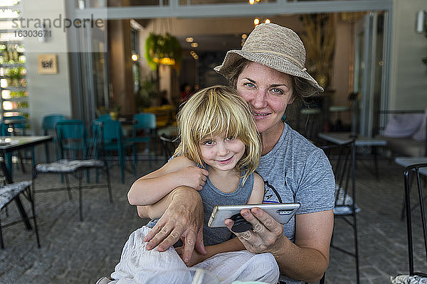 Porträt von Mutter und Tochter  die zusammen im Freien sitzen  mit Smartphone