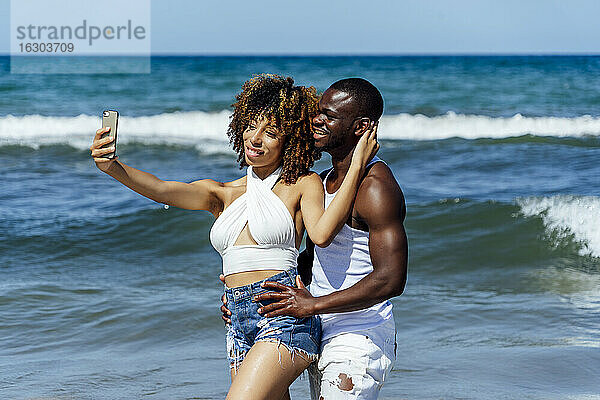 Junge Frau  die ein Selfie mit ihrem Freund macht  während sie im Meer steht