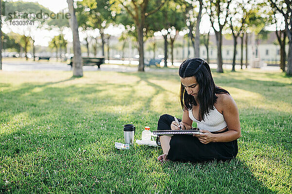 Junge Frau malt Aquarelle in einem Buch  während sie im Park sitzt